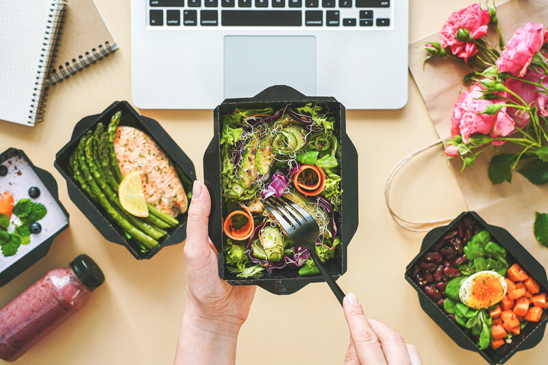 Person isst Mahlzeit aus Box vor Computer