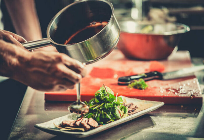 Person träufelt Soße über Fleisch